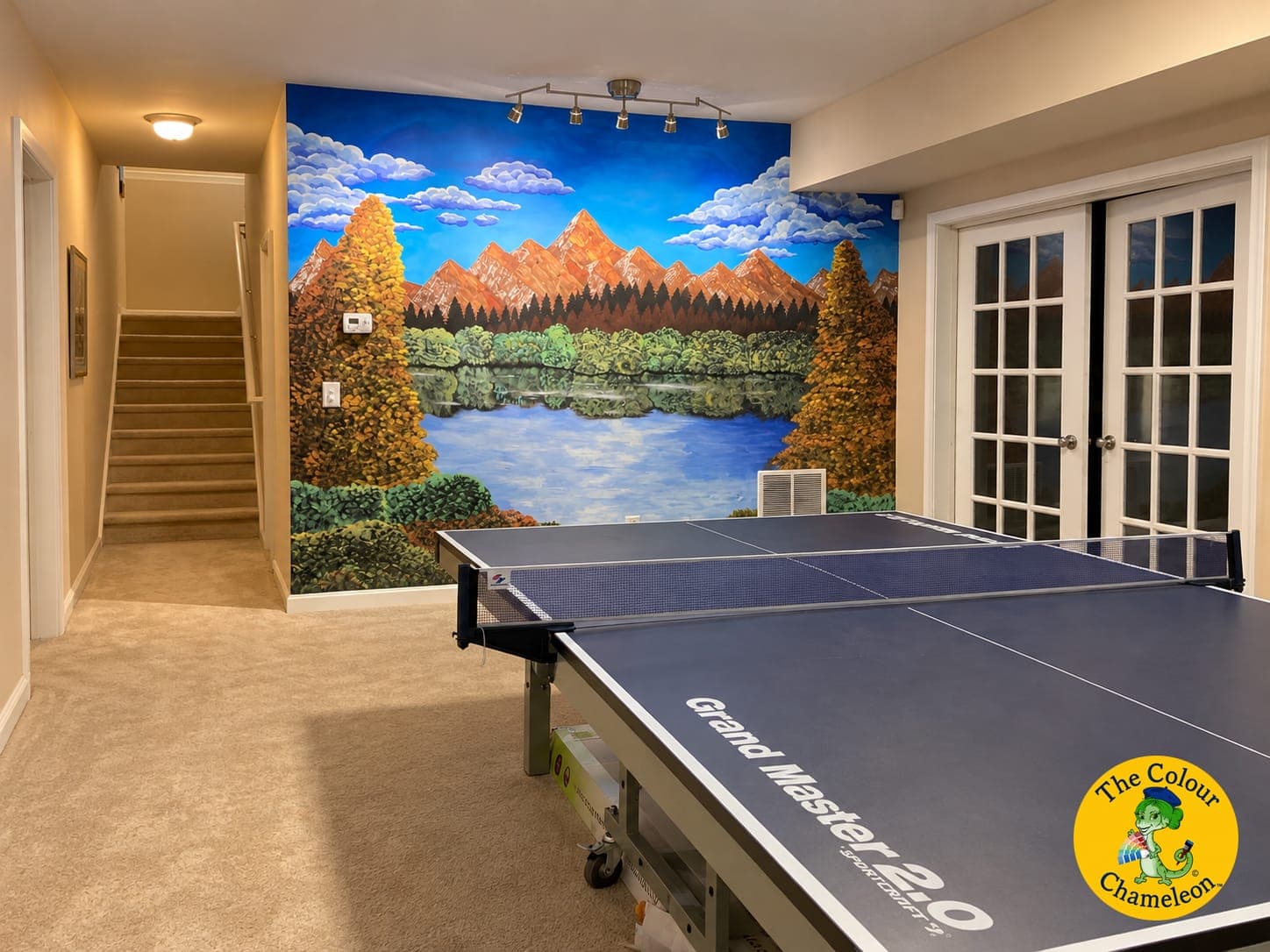 A basement with a painted mountain-and-lake mural on one wall and beige walls elsewhere