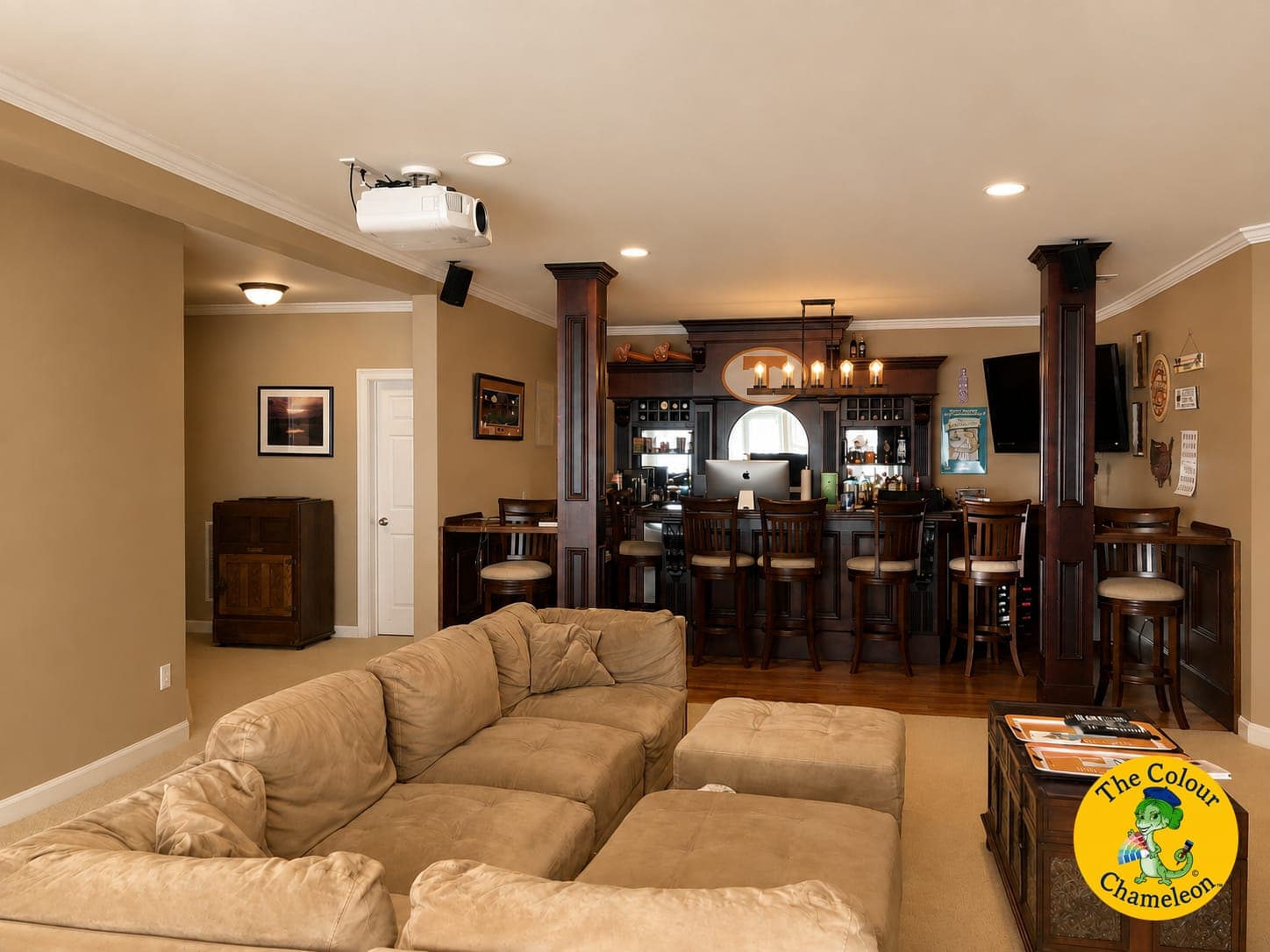 A basement in khaki walls with a beige sectional and a dark wood bar