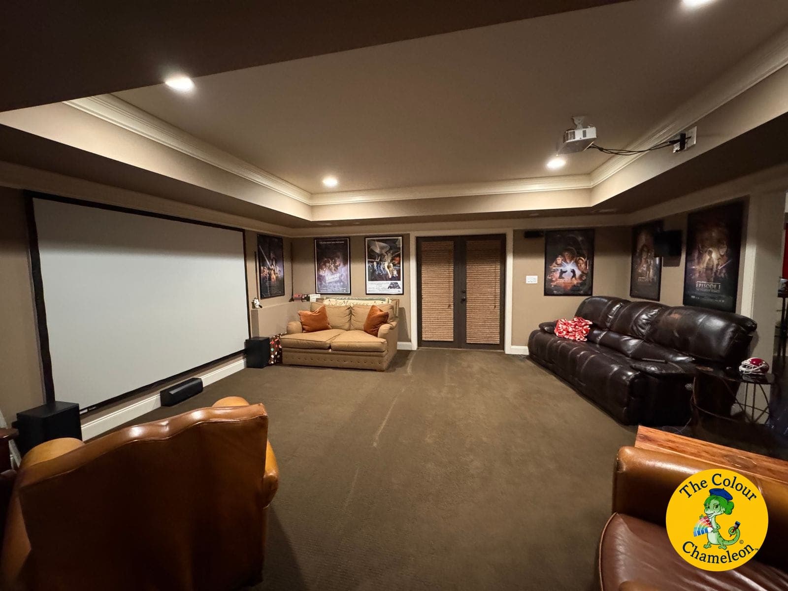The same room in deeper brown as a film room, framed posters flanking a larger screen
