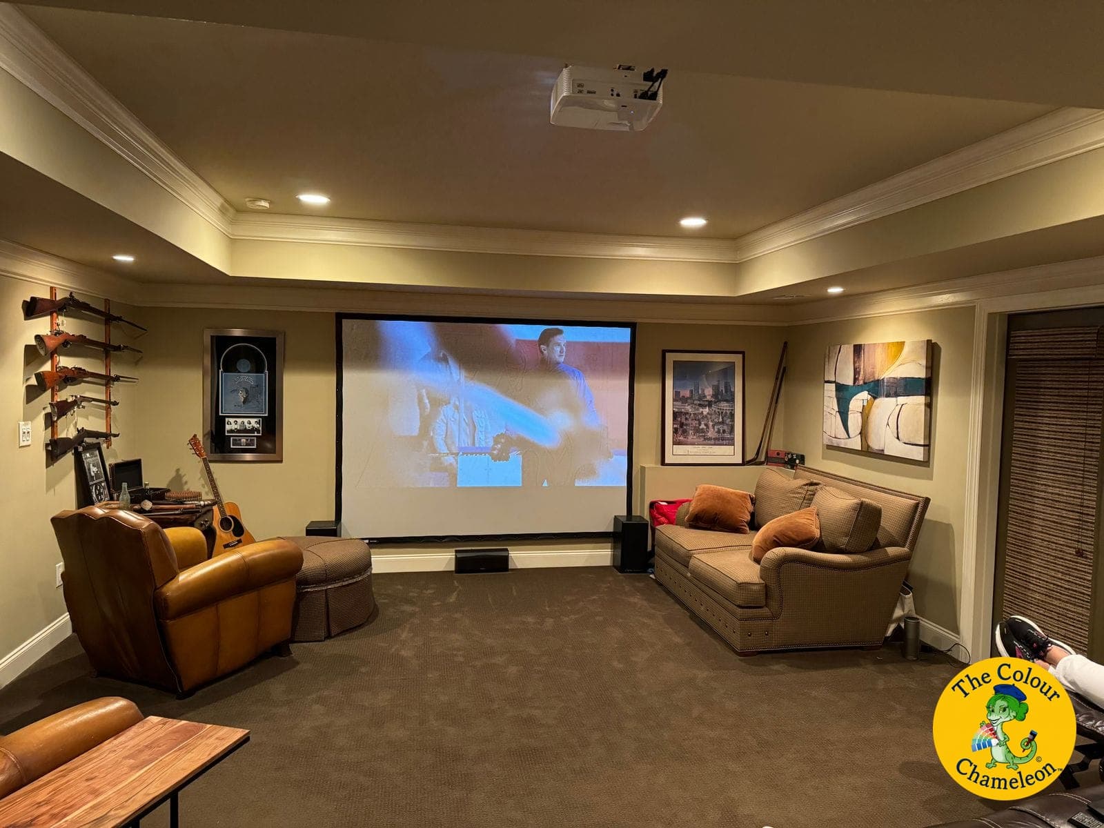 A basement family room in flat tan with a projection screen and guitars on the wall