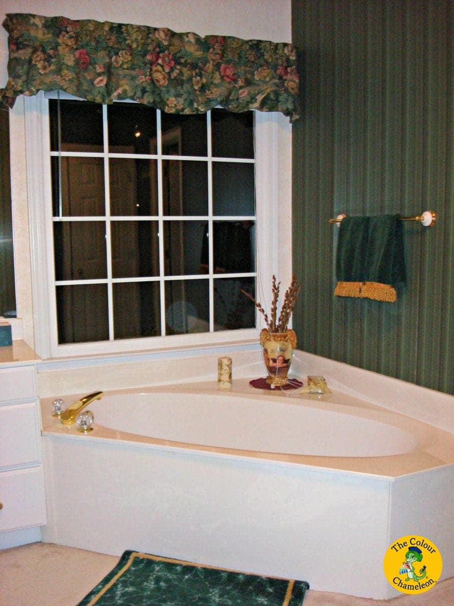 A bathroom in dark green striped wallpaper with a floral valance and a white garden tub