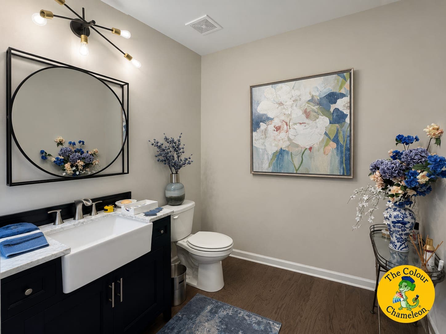 A powder room with greige walls, a black-framed round mirror and a navy vanity