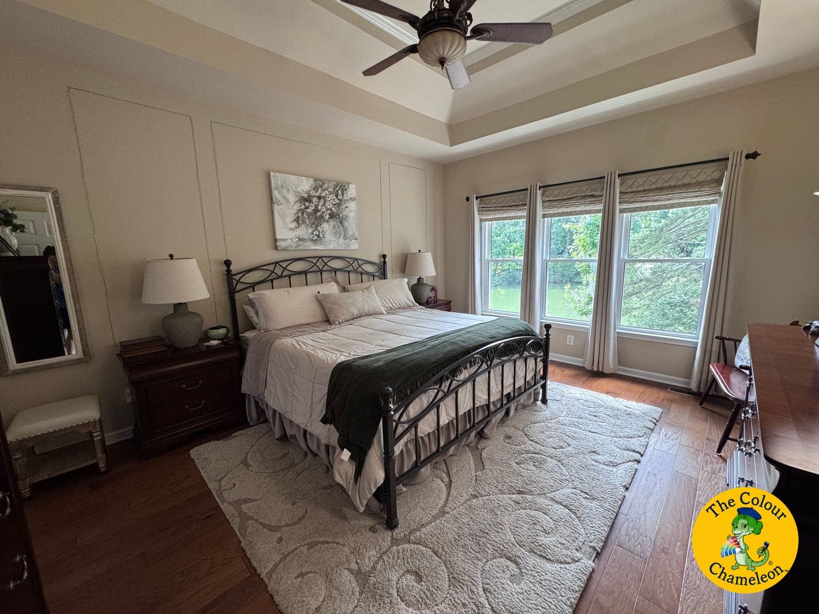 A bedroom with flat beige walls, a tray ceiling and an iron bed