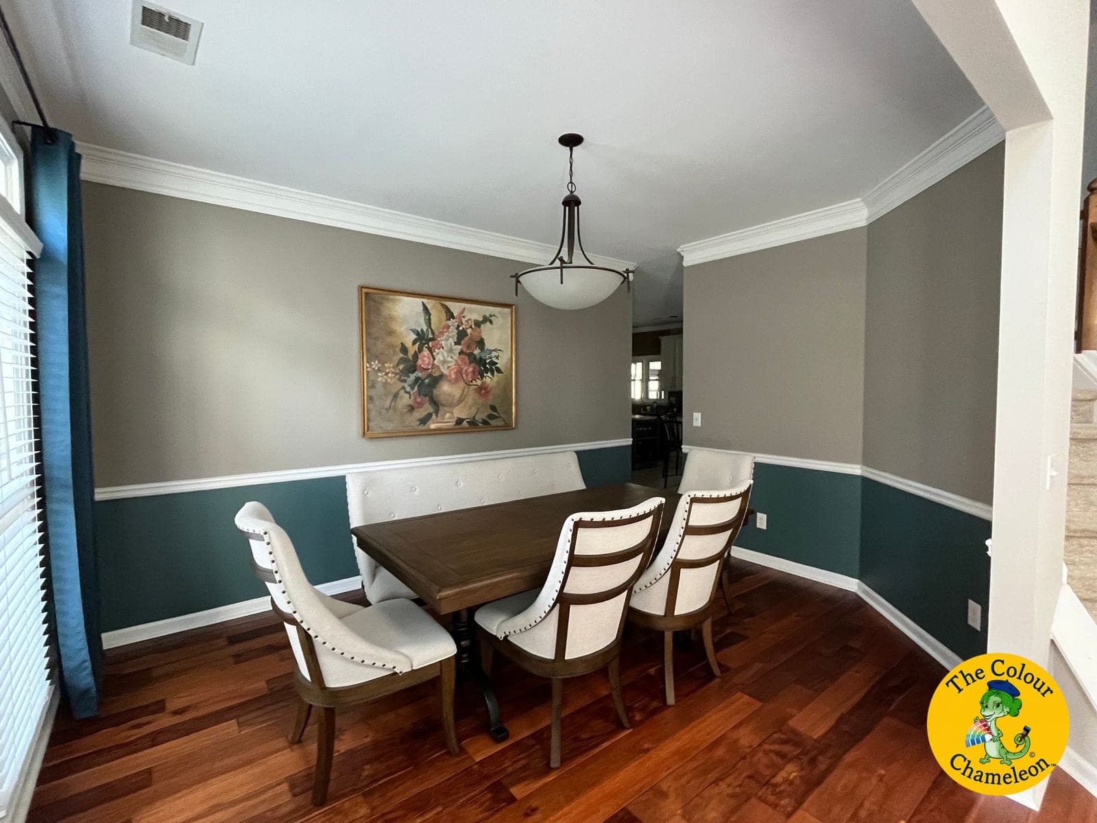 A dining room split by a white chair rail, taupe above and dark teal below