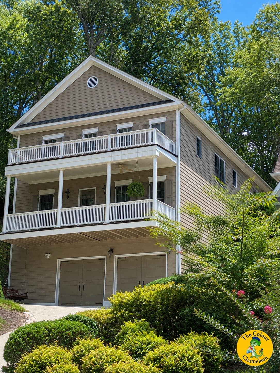 A tall hillside house in neutral taupe siding with white porch railings