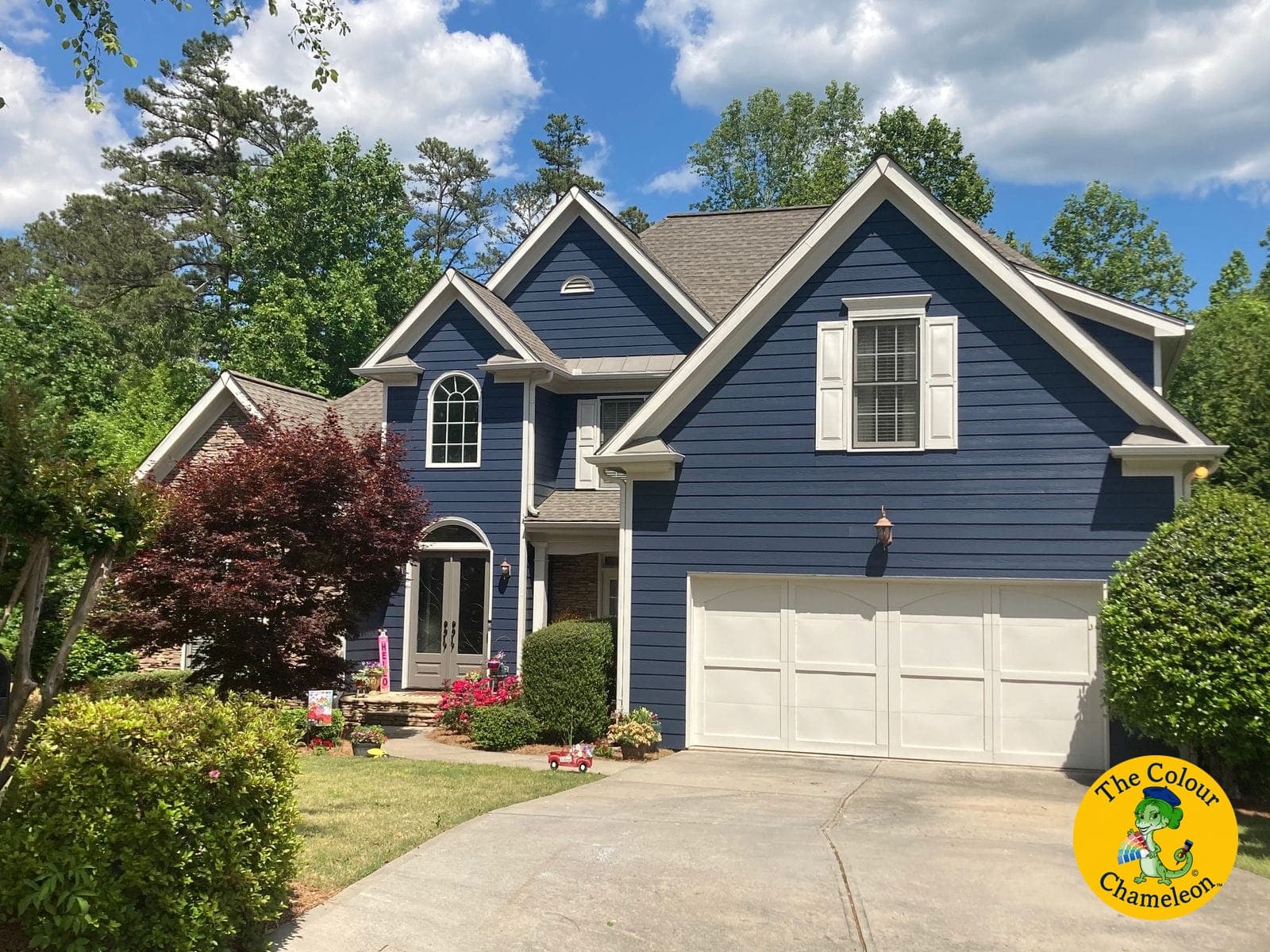 The same house in deep navy siding with crisp white trim, shutters and garage door, the stone and roof unchanged