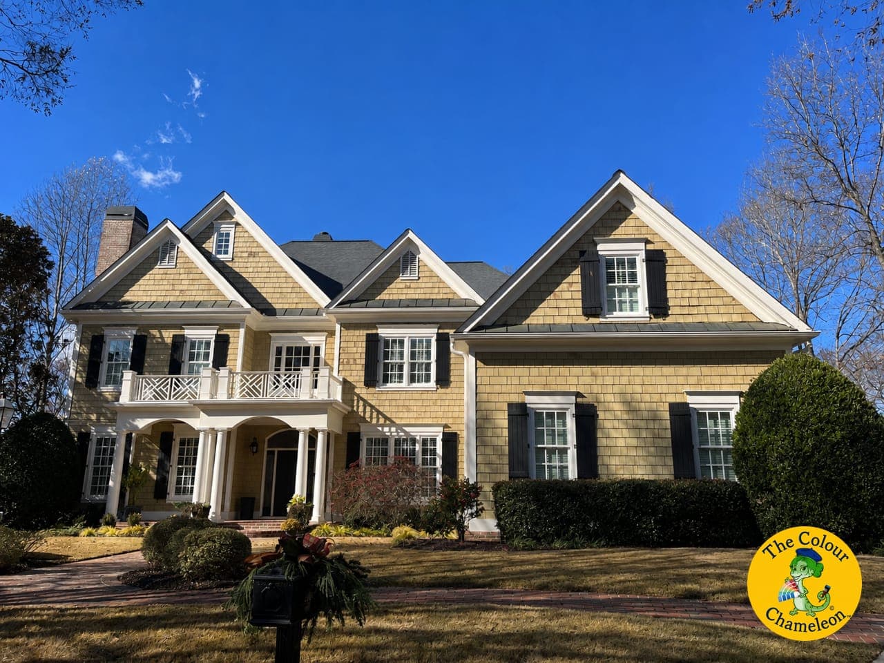 A colonial with yellow shingle siding, black shutters and white porch columns