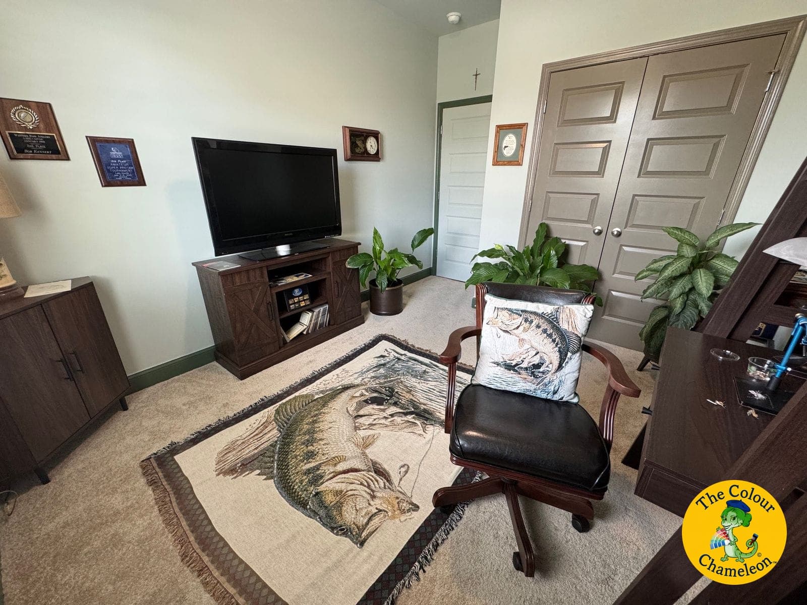 The same room as an office in soft green, with a bass-print rug, dark wood furniture and framed plaques