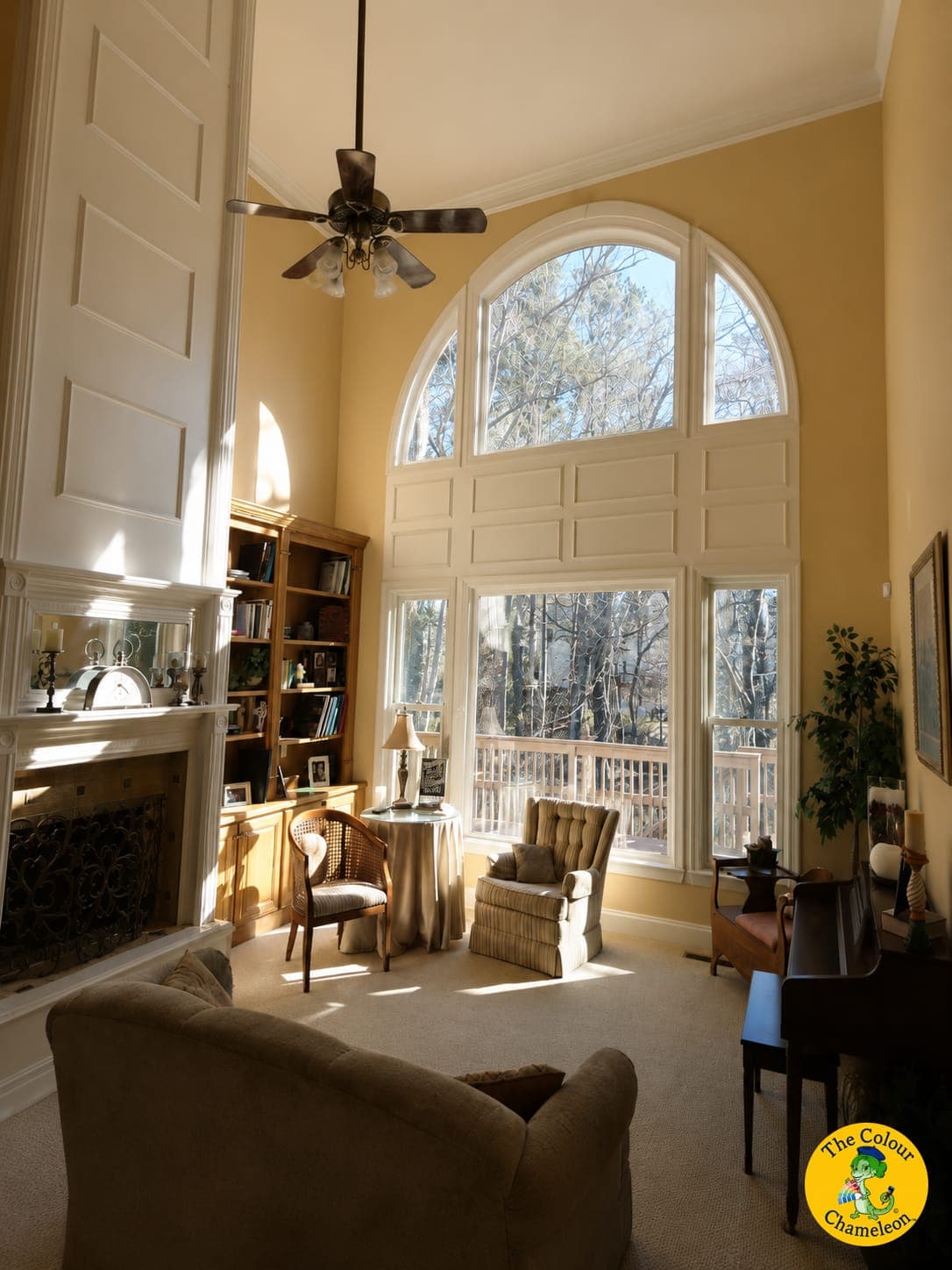A two-story living room in gold walls with an arched window and built-in shelves