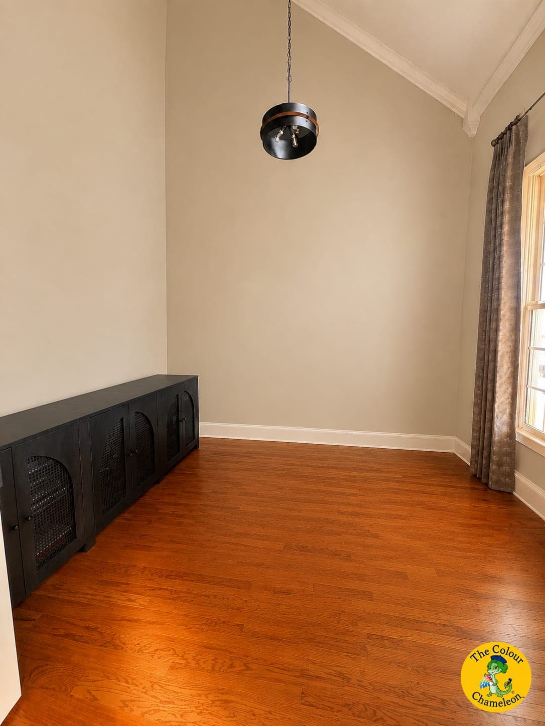 An empty vaulted room in flat beige with a dark credenza and wood floors