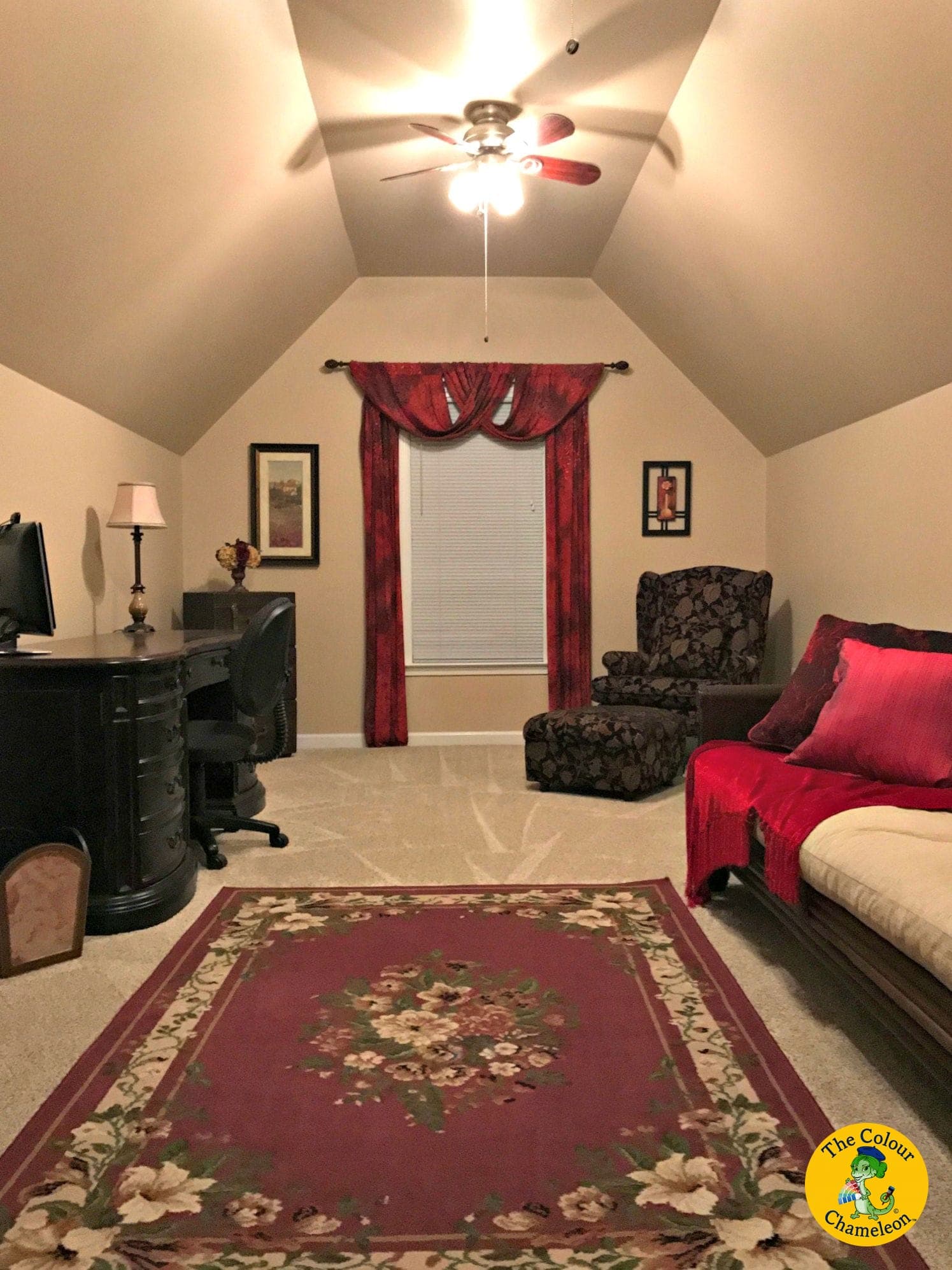 The same room as a guest office in warm beige, with a dark desk, red drapery and a futon